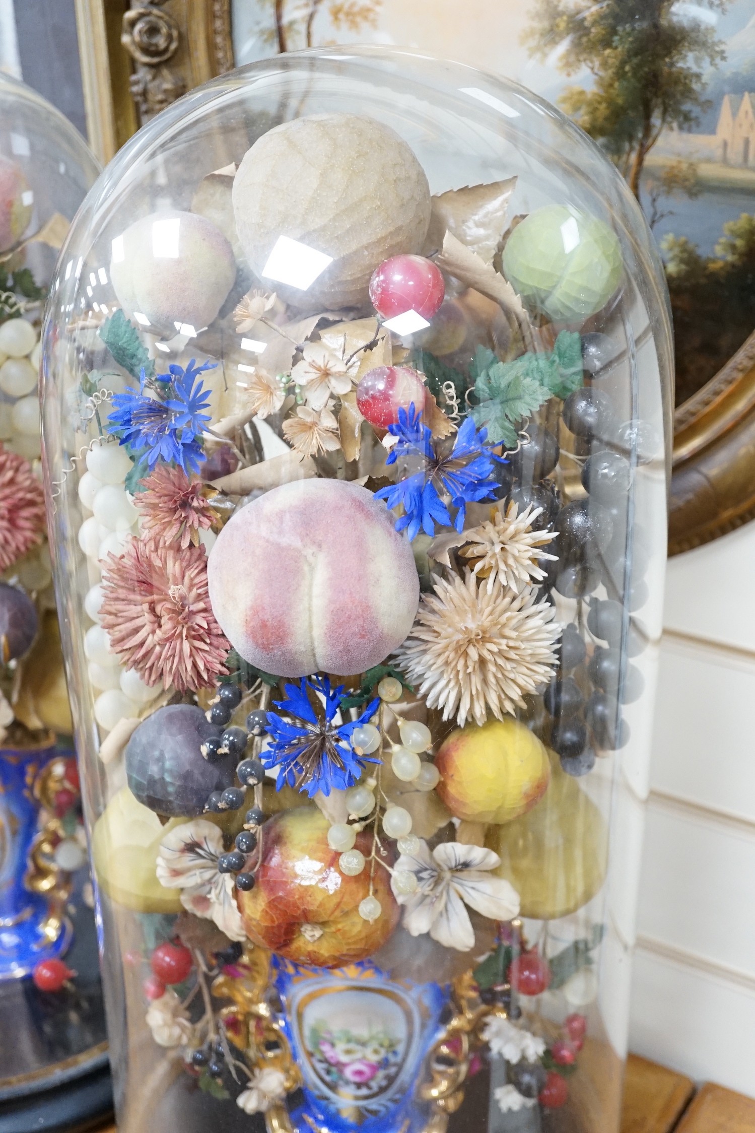 A pair of Victorian displays of painted papier mache fruit in vases, under glass domes, 58cms high